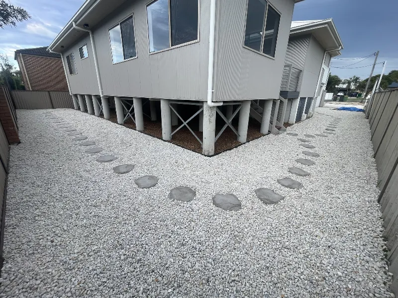 Elevated house on concrete stilts with a gray gravel yard and a curved stepping-stone path around the building.